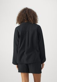 Schwarzes, strukturiertes Langarmhemd mit Kragen und einem lässigen Schnitt. Kombiniert mit passenden Shorts für einen abgestimmten Look.
