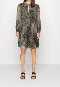 Vestito grigio a fantasia con maniche lunghe, scollo a chiave e vita regolabile con cordino. Abbinato a sandali neri con cinturini.