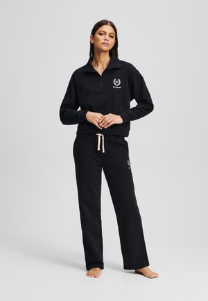 SchwarzFleece-Sweatshirt mit einem Viertel-Reißverschluss-Kragen und besticktem Logo, kombiniert mit passenden schwarzen Jogginghosen und einem beigen Kordelzug.