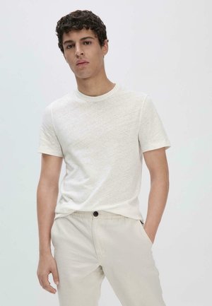 T-shirt grigio chiaro con scollo rotondo, maniche corte e tessuto strutturato. Abbinato a pantaloni beige chiaro con chiusura a bottone.