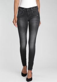 Vaqueros skinny negros con un acabado desgastado, que cuentan con cierre de botón, bolsillos frontales y un ajuste elegante, combinados con tacones altos negros.
