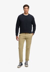 Marineblå struktureret sweater, khakifarvede slim-fit bukser og marineblå sneakers. Trøjen har rund hals, og bukserne har op-rullede manchetter.