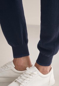 Marina fleece joggers med ribbade muddar i kombination med vita låga sneakers, som visar en mjuk yta och minimalistisk design.