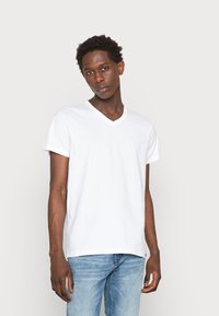 Camiseta de algodón blanco con escote en pico, de mangas cortas, corte relajado y textura suave, combinada con jeans de color azul claro. Diseño liso, sin patrones.