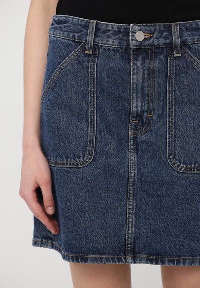 Saia de ganga com cintura alta, comprimento até meio da coxa, dois bolsos frontais e costura em contraste. Cor azul escura com textura desbotada.