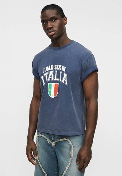 Μπλούζα από βαμβάκι σε ναυτικό μπλε με γυρισμένα μανίκια, με λευκό κείμενο και σχέδιο ασπίδας με τα χρώματα της ιταλικής σημαίας (πράσινο, άσπρο, κόκκινο).