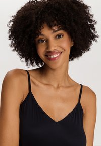 Camiseta negra de tirantes finos, con escote en V y borde de volante, hecha de una tela suave y lisa. Diseño ajustado.