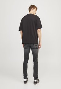 T-shirt noir à manches courtes avec une coupe décontractée, associé à un jean slim gris foncé avec des poches arrière cousues et des chaussures noires.