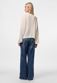Lightweight, cream-colored sweater with long, slightly billowed sleeves and a cropped hem, paired with loose-fitting, dark-wash denim jeans.