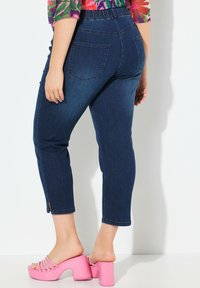 Dżinsowe spodnie capri z elastycznym pasem, z dwoma tylnymi kieszeniami i lekko dopasowanym krojem. Noszone z różowymi, masywnymi sandałami na obcasie.