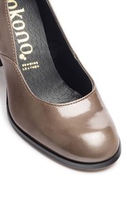 Scarpa in cuoio marrone chiaro con finitura lucida, punta rotonda e lati aperti. Presenta una fodera interna nera e una suola nera. Logo dorato visibile.