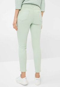 Jeans skinny verde menta con una texture liscia, tasche laterali e vita alta, abbinati a sneakers bianche.