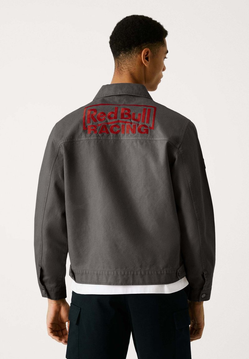 Graue Baumwolljacke mit einem auffälligen roten gestickten "Red Bull RACING" Logo auf dem Rücken. Klassischer Kragen und Knopfmanschetten.