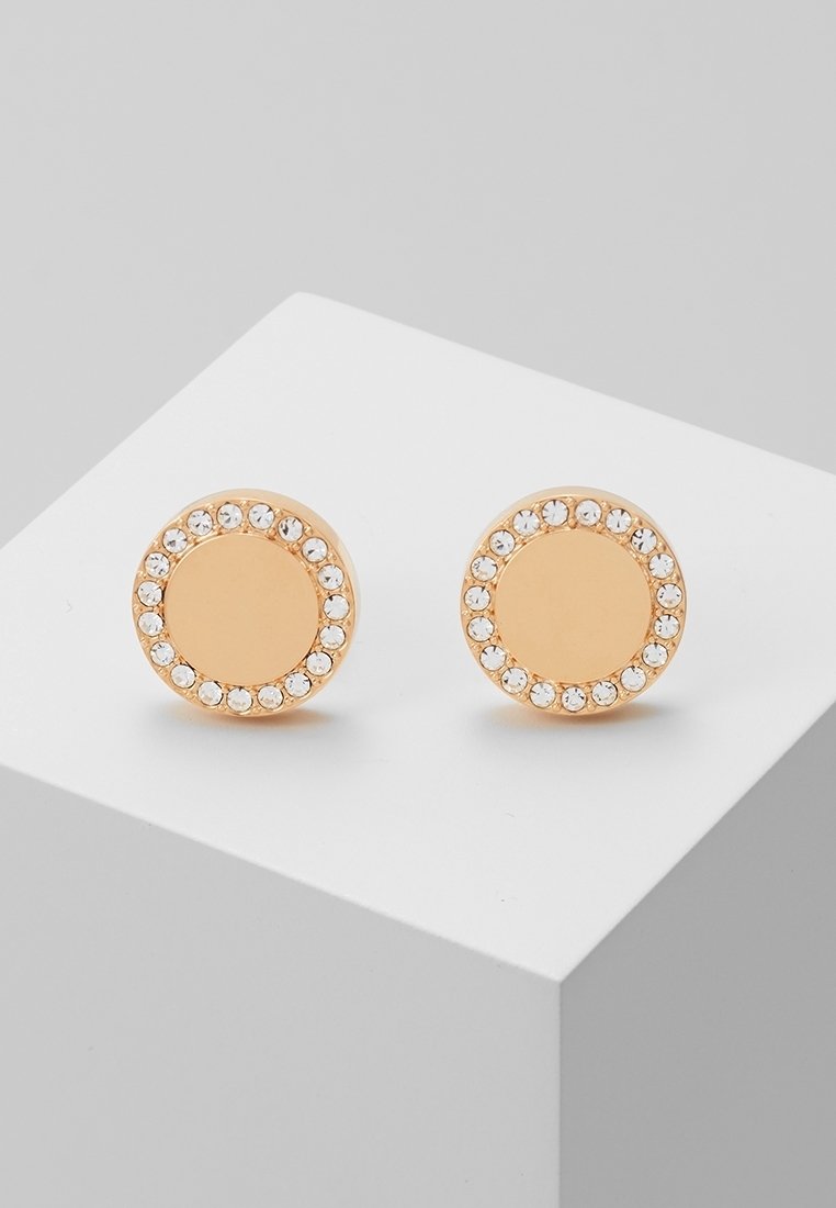 Boucles d’oreilles clous rondes en or avec une bordure de petits cristaux clairs, présentées sur une surface blanche inclinée.