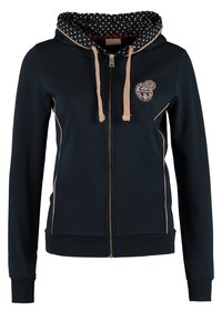 Sweat à capuche zippé bleu marine avec cordons beiges, poignets et ourlet côtelés, petit logo brodé sur la poitrine et doublure intérieure de capuche à motifs.