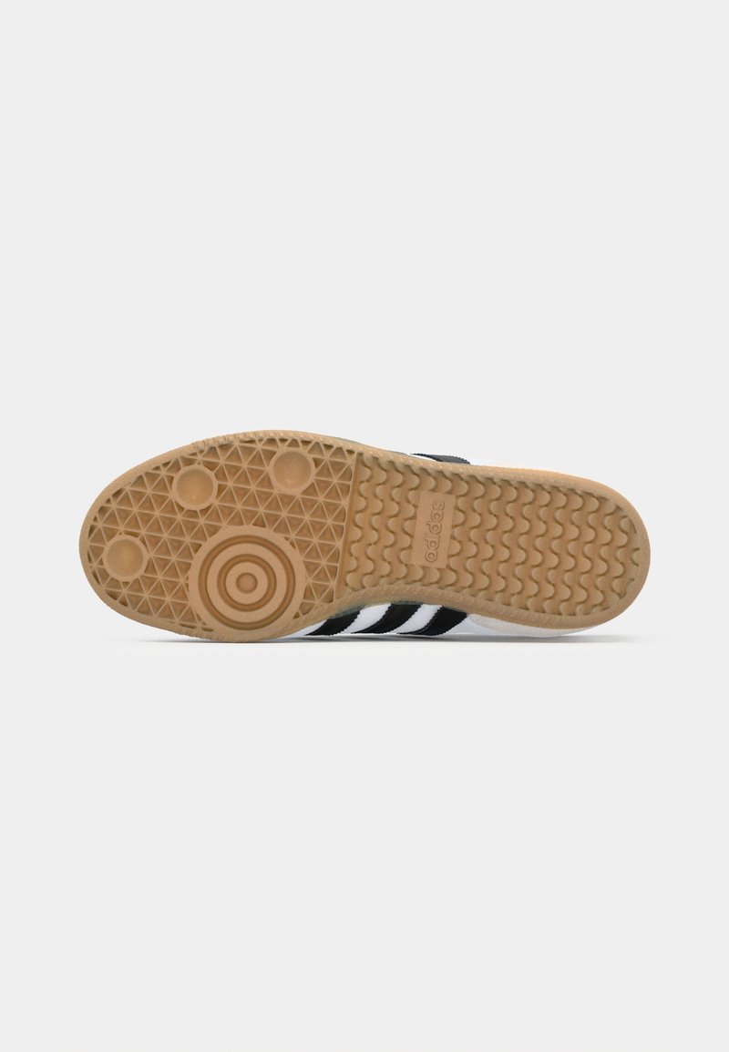 Sohle eines schwarz-weißen Adidas Sneakers mit Gummilaufsohle, kreisförmigen und gewellten Profilmustern sowie dem Adidas-Logo im Fersenbereich.