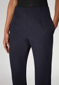 Marineblå skræddersyede bukser med en glat tekstur, slank pasform, sidelommer og et rent taljedesign. Stoffet fremstår let og alsidigt.