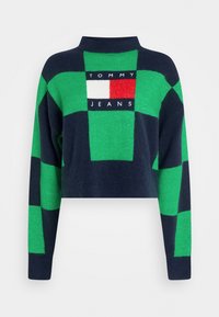 G Kürzer Pullover in Navyblau, Grün und Rot. Besitzt ein Schachbrettmuster mit einem Logopatch in der Mitte, auf dem "TOMMY JEANS" steht.