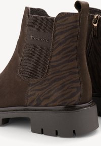 Brązowe zamszowe botki za kostkę z elastycznymi panelami bocznymi i teksturowanym wzorem w paski zebry. Masywna gumowa podeszwa i zamek błyskawiczny z boku.