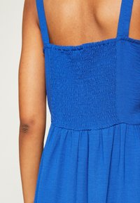 Vestido azul con cuerpo fruncido y tirantes finos. La tela es ligera con una textura suave y un diseño de falda fluida.