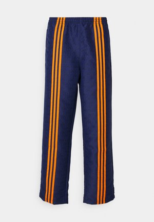 Blå treningsbukser med et heltrykt mønster og oransje striper på sidene, med en komfortabel elastisk midje og løs passform.