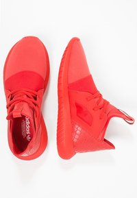 Červené sportovní boty s horním dílem z jemné síťoviny a syntetického materiálu, texturovanými akcenty, kulatou špičkou a gumovou podrážkou. Obsahují šněrování a polstrovaný límec.