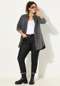 Camicia di denim grigia con spalle borchiate, maniche lunghe, top senza maniche bianco sotto, jeans neri, risvolti alle maniche e stivali neri alla caviglia.