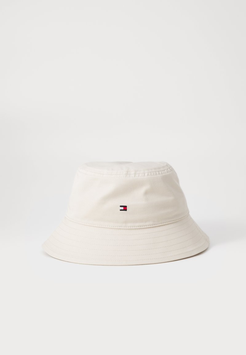Cappello a secchiello beige chiaro realizzato in cotone. Presenta un visiera cucita, un logo laterale nei colori rosso, bianco e blu, e una texture liscia.