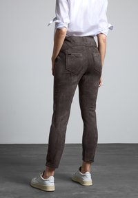 Bruine suède-achtige high-waisted broeken met een getailleerd ontwerp, achterkant zakken en een gladde textuur, gecombineerd met witte sneakers op grijze vloer.