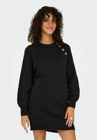 Zwarte gebreide jurk met een ronde halslijn, lange pofmouwen, zijslits en drie decoratieve gouden knopen op de linkerschouder.