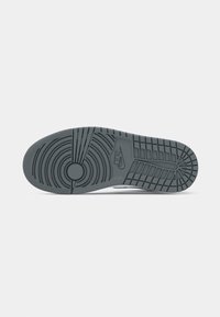 Semelle de sneaker en caoutchouc gris avec des motifs de bande de roulement circulaires et linéaires. Présente un cercle proéminent au centre et un logo en relief sur le côté.