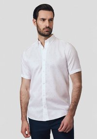 Biała koszula z krótkim rękawem z kołnierzykiem zapinanym na guziki, ozdobiona wzorem małych niebieskich kropek. Gładka tkanina i standardowy krój.