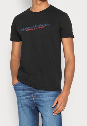 T-shirt en coton noir avec un col rond et des manches courtes. Texte rouge et bleu "Diesel Industry Denim Division" affiché sur le devant.
