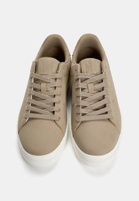 Beige tenisice s glatkom, mat površinom, s ravnim vezicama, minimalnim šavovima i bijelim gumenom potplatom. Imajú zaobljen nos i podstavljeni ovratnik.