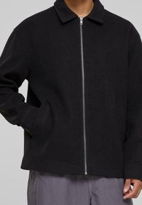 Svart ull zip-up jacka med krage, sidofickor och avslappnad passform. Slät textur och minimalistisk design, lämplig för lager på lager.