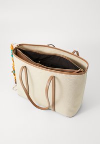 Beige canvas tote bag with brown leather handles, open top, and inner black lining. Features zipper pocket and colorful bead accents.