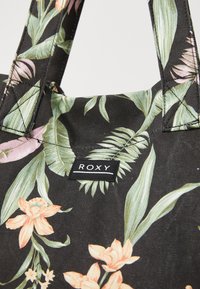 Sac fourre-tout en tissu noir avec un imprimé floral comportant des fleurs orange et rose, des feuilles vertes, et une étiquette logo "ROXY" sur le côté.
