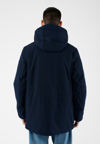 Giacca con cappuccio blu navy dal texture morbido, vestibilità rilassata e maniche lunghe. Presenta una fessura sul retro e dettagli di cucitura discreti.
