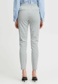 Grå stretchbyxor med slim fit, featuring ett elastiskt midjeband och två bakfickor, i kombination med en blårandig skjorta.
