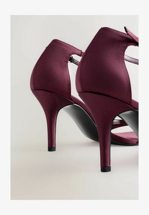 Zapatos de tacón alto de satén burdeos con un diseño elegante, parte posterior abierta y suela negra, con un tacón delgado y puntiaguado y tiras entrelazadas.