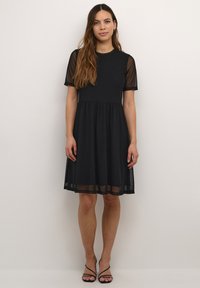 Crna haljina s uskim korzetom, lepršavom suknjom, kratkim prozirnim rukavima i opuštenim siluetom. Glatka tkanina s prozirnim detaljima na rukavima.