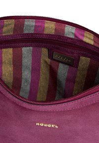 Burgundy suede bag interior with multicolored striped lining in gold, pink, gray, and purple; features a gold logo tag and zip closure.