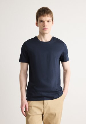 Tricou din bumbac moale, de culoare bleu marin, cu mânecă scurtă; are un decolteu rotund și o siluetă ajustată. Asortat cu pantaloni bej.