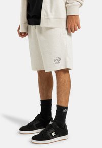 Light grey cotton shorts with side pockets and DC logo in black. Paired with black sneakers and ribbed black socks. Casual fit.