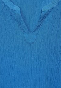 Blau strukturierter Oberteil mit einem V-Ausschnitt und subtilen vertikalen Falten im gesamten Stoff, die der Gesamtgestaltung Tiefe verleihen.