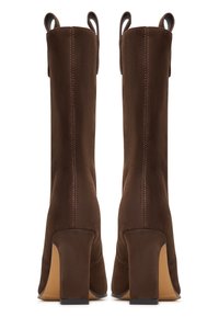 Hnědé semišové kozačky sahající ke kolenům s blokovým podpatkem, vybavené zadními poutky a kontrastním šitím podél švů. Hladk�á textura a strukturovaný tvar.