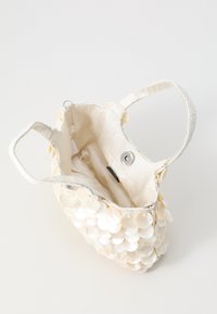 Cream fabric bag with circular shell accents, open top, and two fabric handles. Lined interior features a magnetic snap closure and pocket.