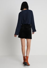Marineblouse met lange mouwen, een flowy design. Zwarte fluwelen minirok, gladde textuur. Bruine enkellaarsjes met hakken met een glanzende afwerking.