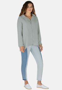 Helles grünes Button-up-Shirt mit langen Ärmeln, kombiniert mit hellblauen und dunkelblauen zweifarbigen Skinny-Jeans und weißen Slippern.