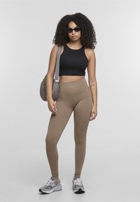 Leggings ajustados en marrón claro, combinados con un top corto negro. Lleva gafas de sol negras y lleva un bolso gris acolchado, con zapatillas gris.
